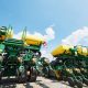 Large green and yellow row crop planters parked outdoors under a blue sky with white clouds.