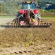 A tractor plows a field, turning over soil with a plow attachment, showcasing agricultural activity.