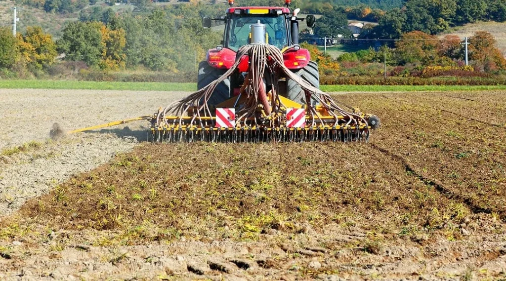 Un tracteur laboure un champ, retournant la terre avec une charrue, illustrant ainsi l'activité agricole.