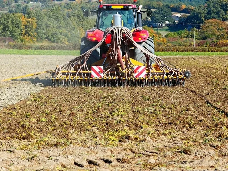 Un tracteur laboure un champ, retournant la terre avec une charrue, illustrant ainsi l'activité agricole.