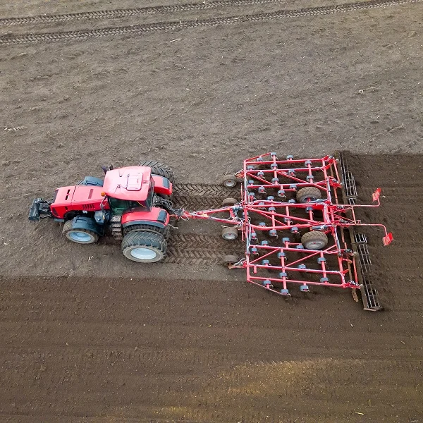 A tractor plowing a field, with soil being turned over and a clear blue sky in the background.